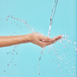 Hands, water and woman in studio with natural, wellness or health routine for self care in morning. Beauty, hygiene and female person with liquid splash in palm for washing skin by blue background.