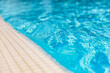 Natural sunlight blur bokeh white marbles closeup of swimming pool edge and clear blue water. New modern swimming pool entrance steps down, clean fresh refreshing blue water on bright hot summer day