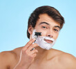 Portrait, razor and man shaving in studio for hair removal, hygiene or grooming for health isolated on blue background. Cream, face and model cut beard for skincare, beauty and cleaning for wellness