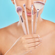 Creative, makeup and girl with brushes in hand for application of cosmetics in blue background. Studio, beauty and artist with tools to apply foundation, powder or product in skincare with smile