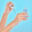 Hands, skincare and person with serum bottle in studio for glow or wellness on blue background. Product, closeup and model with hyaluronic acid, essential oil or cosmetics for aesthetics and beauty