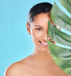Woman, portrait and palm leaf with skincare glow from spa treatment and natural cosmetics. Model, skin and face of person relax for dermatology detox in a studio with blue background feeling healthy