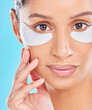 Woman, beauty and eye patches with skincare glow from spa treatment and cosmetics. Model, hand and face of a person relax after dermatology detox in a studio with blue background feeling healthy