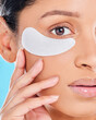 Woman, portrait and eye patches with skincare glow from spa treatment and cosmetics. Model, hand and face of a person relax after dermatology detox in a studio with blue background feeling healthy