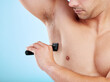 Shaver, underarm and man in studio for hair removal, depilation or grooming treatment for hygiene. Self care, health and closeup of male person with razor for body wellness by blue background.