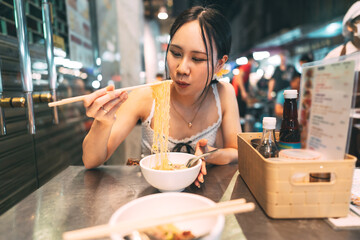 Wall Mural - Asian foodie tourist woman eating wonton noodles at China town asia street food night market