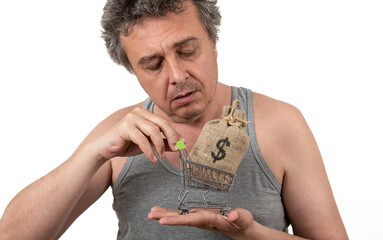 Wall Mural - A shaggy gray-haired unshaven man in a sleeveless T-shirt holds a miniature shopping cart from a supermarket and a money bag with a US dollar symbol