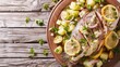 Fish and potato salad with roasted fish topped with onion and lemon slices for garnish on a wooden table from above