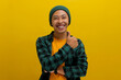 A smiling young Asian man, dressed in casual clothes and wearing a beanie hat, is giving a thumbs up gesture, indicating a positive or good review while standing against a yellow background