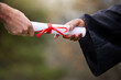Student, hands and giving diploma for graduation in outdoor, learning award and achievement. Person, academy degree and college or university success, scroll and certificate at outside ceremony