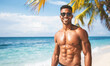 A man with a six pack of abs is smiling and posing for a picture on a beach
