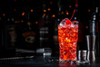 © 5ph - Red cocktail drink with pink vermouth, liqueur, cherry, juice and ice, black bar counter background, steel tools and bottles
