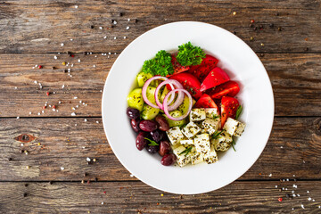 Poster - Greek style salad - fresh vegetables with feta cheese and kalamata olives served in white bowl on wooden table
