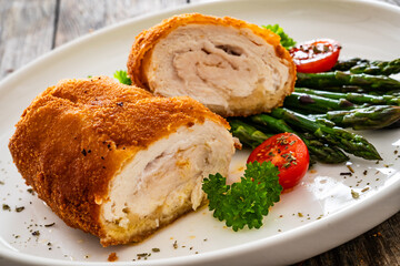 Wall Mural - Cutlet de Volaille, wrapped chicken cutlet served with cooked green asparagus on wooden table
