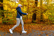Autumnal Nordic walking - mid-adult beautiful woman exercising in city park using  Nordic walking poles
