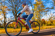 Mid-adult woman riding bicycle in city park in autumnal scenery
