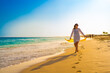 Beautiful woman holding shawl walking on sunny beach
