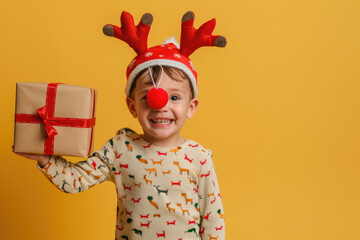 Wall Mural - A cute little boy wearing reindeer antlers on his head, holding up the nose with one hand and carrying gifts in the other, wearing a red Christmas sweater with a deer pattern