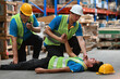 © saltdium - Two workers are helping and ask for help on a walkie-talkie while his co-worker is lying unconscious at an industrial plant. First aid and basic life support concepts for employees