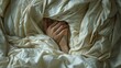 Close-up image of a person peeking out shyly from under a mess of soft white blankets in a cozy bedroom setting.