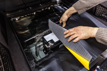 Auto service worker installing soundproofing foam material on car door trim from inside, tuning car sound or installing noise insulation. Process of car sound insulation installation.