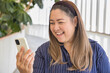 Happy Cheerful smiling Middle aged Asian aunt, aged woman using smartphone with positive expression