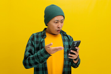 Wall Mural - An unhappy Asian man, dressed in a beanie hat and casual shirt, reacts to a message with bad news on his mobile phone, displaying feelings of sadness, worry, and anxiety, Isolated on yellow background