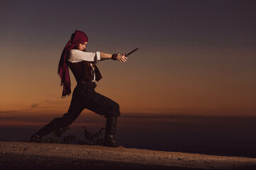 Wall Mural - Outdoor portrait of young female in pirate costume holding a knife. Copy space