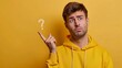 A young man with one hand pointing to the side in the air, where there is a question mark. The man's expression is very puzzled, indicating uncertainty about some issues. Yellow background.





