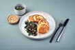 Traditional American pancakes with spinach, pine-nuts and raisins served as close-up on a Nordic design plate with cutlery