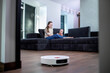 Robotic vacuum cleaner cleaning the living room while mother and son playing