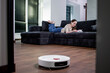 Woman lying on sofa and reading a book while robot vacuum cleaner doing housework