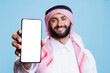 © DC Studio - Man in arabic attire holding smartphone displaying white screen for application advertising. Smiling muslim person posing in studio and showing mobile phone blank touchscreen closeup