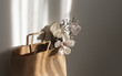 Craft paper bag against white wall with geometrical shadows , gorgeous artificial magnolias in it. Eco friendly concept, copy space for your text.