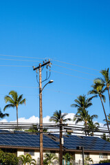 Condo building roof covered in solar panels to generate green alternative energy on sunny Maui, in contrast to the utility power distribution lines in front
