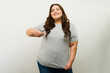 Confident plus-size woman happily showing a mockup t-shirt and pointing at the design in a studio setting
