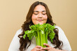 Confident plus-size woman enjoys the scent of fresh green celery in a warm-toned studio setting