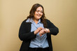 Happy plus-size woman checking the time on a smartwatch in a studio with a simple backdrop