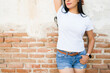 Stylish latina woman in a blank white t-shirt confidently poses against a rustic brick wall, ideal for design mockups and fashion showcases