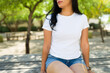 Hispanic woman in a white t-shirt ideal for mockup designs, posing in a natural park setting with trees in the background