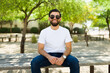 Smiling hispanic man in a white t-shirt and sunglasses sitting on a park bench, ideal for mockups and casual clothing designs