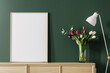 A white poster frame is placed on the sideboard of an olive green wall, with tulips in vases and floor lamps next to it. The scene has a modern minimalist style, with a closeup shot capturing details.
