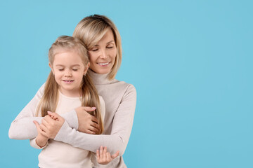 Canvas Print - Mother hugging her happy daughter on light blue background. Space for text