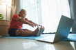 Elderly Asian man practicing yoga at home, following an online tutorial on a laptop