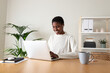 Black female entrepreneur working at home office. Happy African American woman using laptop and wireless earphones.