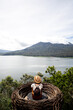 Tourist woman contemplating nature sitting in straw nest looking at lake view and mountains in Bali. Copy space.Vertical