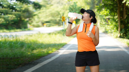 Wall Mural - Healthy athletic asia woman is drinking pure water from the bottle refreshing herself after exercise in the nature park. Healthy and Lifestyle Concept