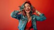 © ORG - Happy young woman dancing and smiling cheerfully while standing against a red background.