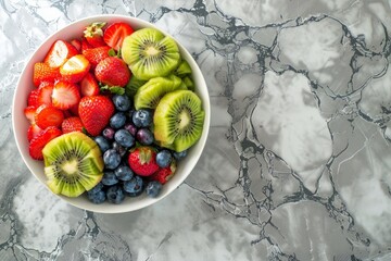 Wall Mural - Fresh strawberries, blueberries, and kiwi slices piled in a white bowl on a marble counter