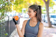 Young pretty sport woman holding an orange at outdoors with happy expression